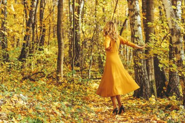 Sarı uzun elbiseli Genç güzel kız düşmüş yaprakları ile sonbahar park içeri girer.