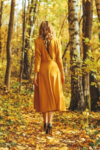 Молода красива дівчина в жовтій довгій сукні гуляє в осінньому парку з опалим листям — стокове фото