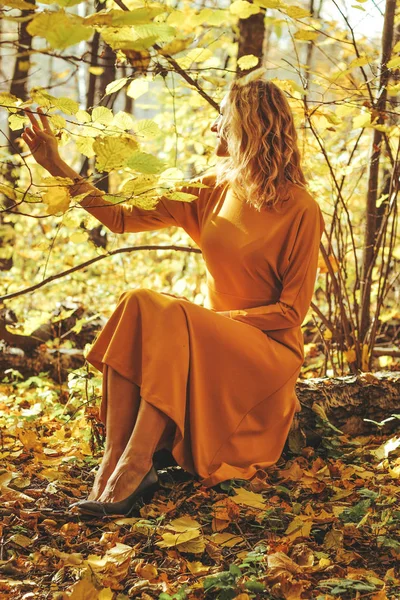 Giovane bella ragazza in un abito lungo giallo passeggiate nel parco autunnale con foglie cadute — Foto Stock