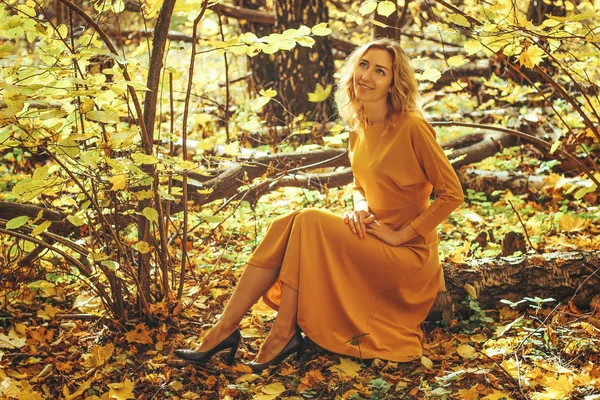 Young beautiful girl in a yellow long dress walks in autumn park with fallen leaves — Stock Photo, Image