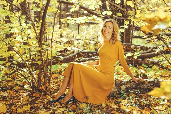 年轻美丽的女孩在黄色长礼服散步在秋季公园与落叶 — 图库照片