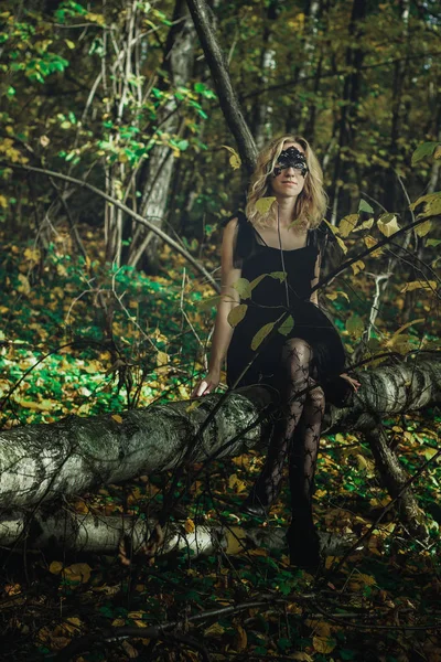 A young kind witch in a black dress with a black mask in a mystical forest in various poses. Art processing.