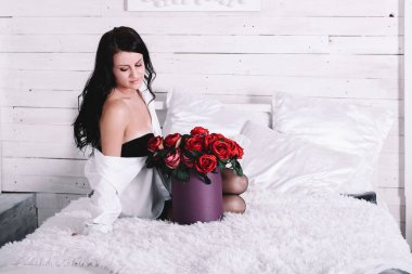 Genç Seksi esmer beyaz gömlekli stüdyo parlak beyaz yatakta yatıyor