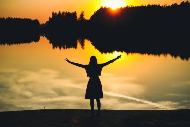 Eller su birikintisi yansıması günbatımında arka plan karşı güzel bir genç kızla silüeti.