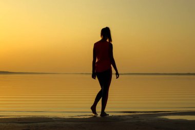 Deniz kıyısı turuncu günbatımı sırasında bir genç güzel kız silüeti.