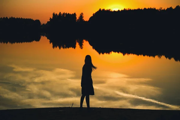 池の反射で夕日の背景に美しい少女のシルエット — ストック写真