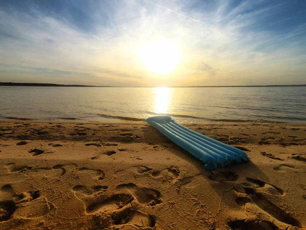 Όμορφη αμμουδιά με γκρο πλαν ίχνη κατά το ηλιοβασίλεμα το καλοκαίρι. Μπλε φωτεινή φουσκωτό στρώμα κινηματογραφήσεων σε φόντο ηλιοβασίλεμα. — Φωτογραφία Αρχείου