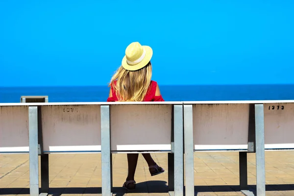 Joven chica atractiva en un vestido rojo sentado en un banco cerca del mar en el verano, Batumi, Georgia — Foto de Stock