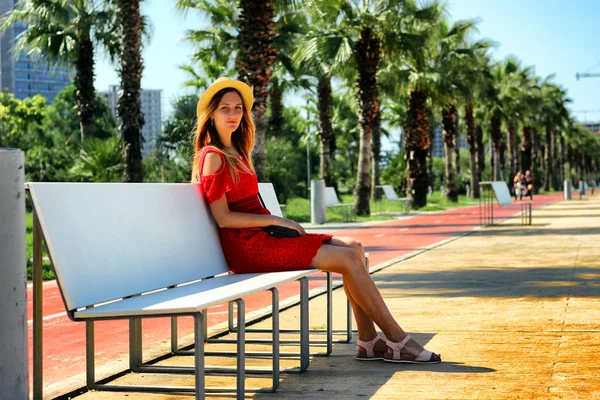 Mladá atraktivní dívka v červených šatech, sedící na lavičce u moře v létě, Batumi, Gruzie — Stock fotografie