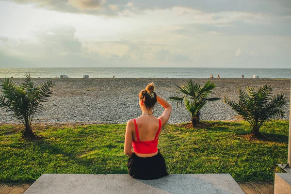 Joven chica atractiva en una camisa roja sentada cerca del mar en el verano, Batumi, Georgia —  Fotos de Stock