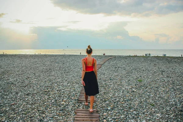 Joven chica atractiva en una camisa roja caminando por la carretera cerca del mar en el verano, Batumi, Georgia —  Fotos de Stock