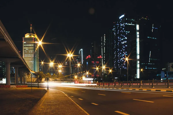 Night city Dubai with glowing light from the road and buildings near the metro station line — Stock Photo, Image