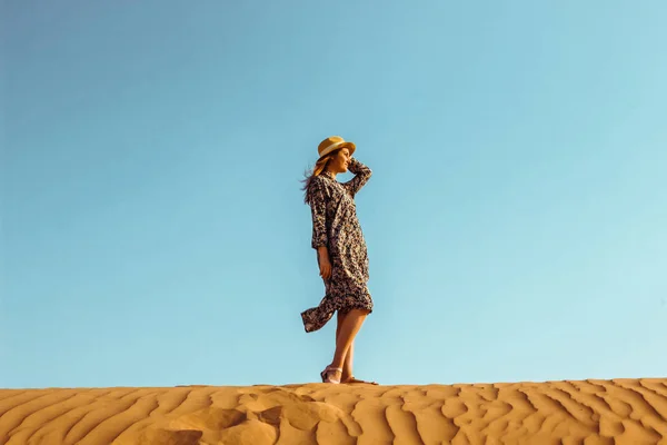 Young beautiful girl in a long dress and a hat in the middle of the desert during the daytime — Stock Photo, Image