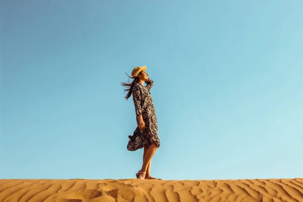 Joven chica hermosa en un vestido largo y un sombrero en el medio del desierto durante el día — Foto de Stock