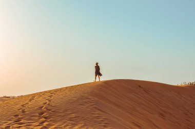 Gündüz vakti çölün ortasında uzun elbiseli ve şapkalı güzel bir kız.