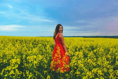 Kırmızı elbiseli güzel bir kız sarı tarlanın ortasına yakın turp çiçeğiyle