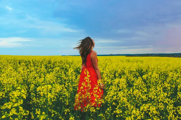 Giovane bella ragazza in un abito rosso da vicino in mezzo al campo giallo con fiore di ravanello — Foto Stock