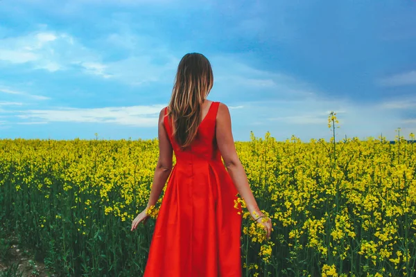 Giovane bella ragazza in un abito rosso da vicino in mezzo al campo giallo con fiore di ravanello — Foto Stock