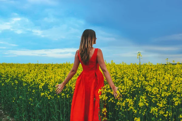 Giovane bella ragazza in un abito rosso da vicino in mezzo al campo giallo con fiore di ravanello — Foto Stock