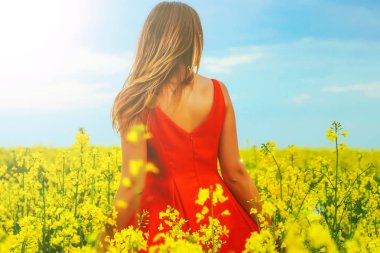 Kırmızı bir elbise genç güzel kız turp çiçekler ve sunligh ile sarı alanın ortasında yakın