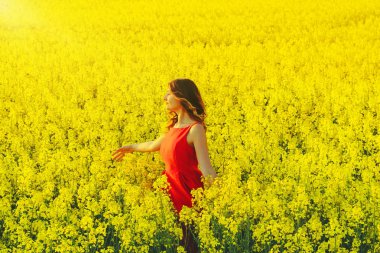 Kırmızı bir elbise genç güzel kız turp çiçekler ve sunligh ile sarı alanın ortasında yakın