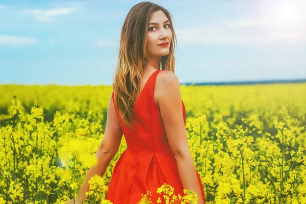 Mladá krásná dívka v červených šatech zblízka uprostřed žlutého pole s květinami a slunečnice — Stock fotografie