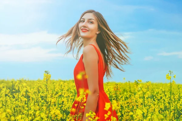 Giovane bella ragazza in un abito rosso da vicino in mezzo al campo giallo con fiori di ravanello e sunligh — Foto Stock