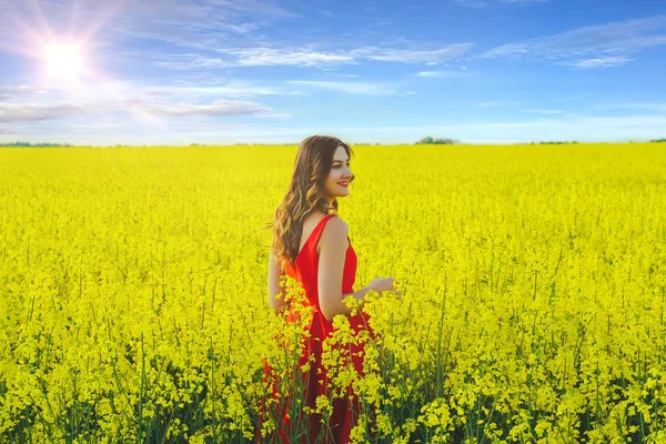 Giovane bella ragazza in un abito rosso da vicino in mezzo al campo giallo con fiori di ravanello e sunligh — Foto Stock