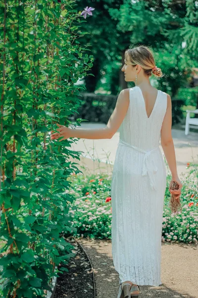 Młoda piękna kobieta w białej sukni w zielonym ogrodzie z kwiatami z bliska w okresie letnim — Zdjęcie stockowe