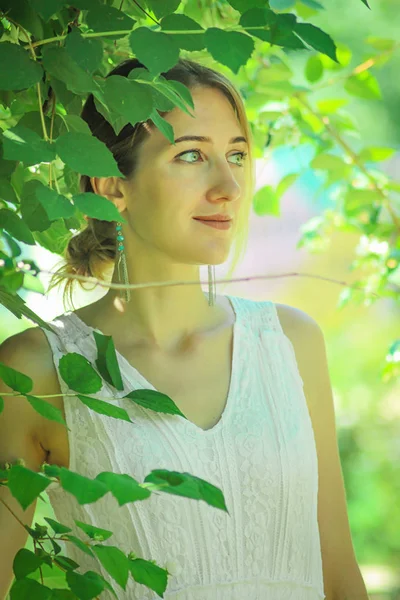 Giovane bella ragazza in un abito bianco primo piano sullo sfondo di cespugli verdi con gelsomino fiorito — Foto Stock