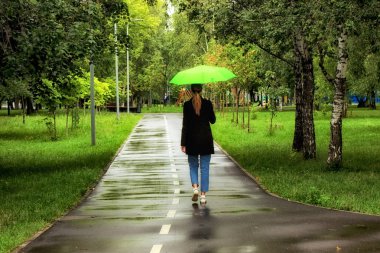 Genç güzel kız yaz aylarında şehir parkında yeşil şemsiye altında tek başına yürüyüş