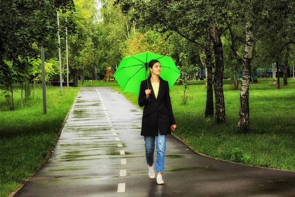 Ung vacker flicka som går ensam under grönt paraply i stadsparken på sommaren — Stockfoto