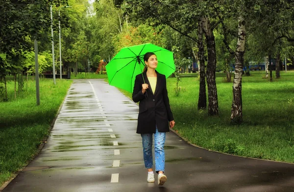 Ung vacker flicka som går ensam under grönt paraply i stadsparken på sommaren — Stockfoto