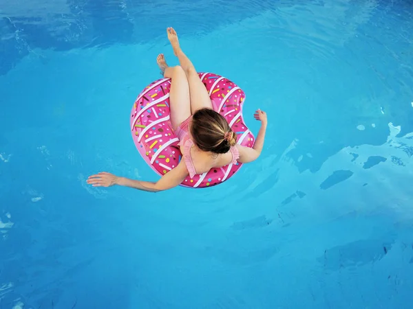 Menina bonita jovem relaxante e nadando na piscina azul com um círculo rosa close-up . — Fotografia de Stock