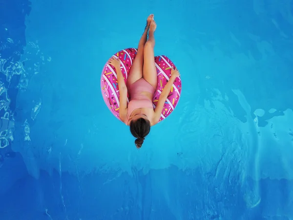 Menina bonita jovem relaxante e nadando na piscina azul com um círculo rosa closeu — Fotografia de Stock