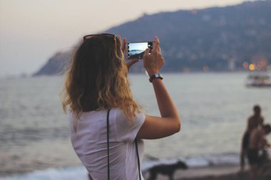 Genç güzel kadın cep telefonunuzda gün batımında Alanya'nın fotoğrafını cep telefonunuzla yakın çekimde çekiyor