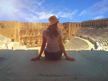 Şapkalı genç güzel kadın yakın oturuyor ve yaz aylarında Amfitiyatro Aspendos manzarasının tadını çıkarıyor