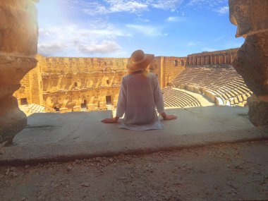 Şapkalı genç güzel kadın yakın oturuyor ve yaz aylarında Amfitiyatro Aspendos manzarasının tadını çıkarıyor