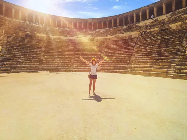 Giovane bella donna è in piedi nel mezzo dell'anfiteatro Aspendos con le mani in alto — Foto Stock