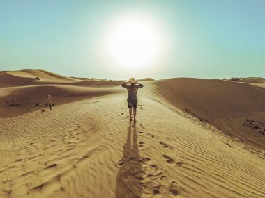 Uzun elbiseli genç güzel kadın Dubai çölükum tepeleri boyunca yürüyor