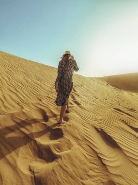 Uzun elbiseli genç güzel kadın Dubai çölükum tepeleri boyunca yürüyor
