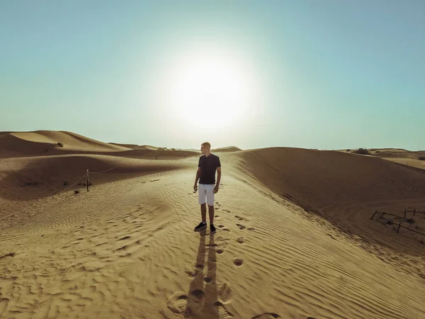 Joven hombre hermoso camina a lo largo de las dunas de arena del desierto de Dubai — Foto de Stock