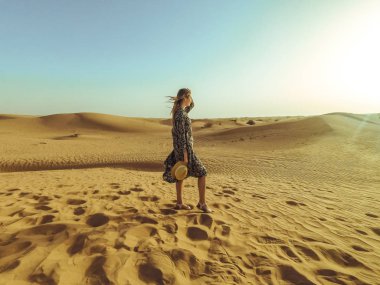 Uzun elbiseli ve güneş ışığı ile Dubai çölün ortasında bir şapka ile genç güzel kadın