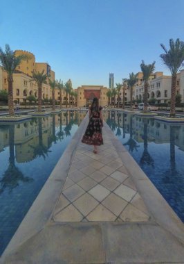 Downtown Burj Dubai bölgesi yakınlarındaki yüzme havuzu boyunca yolda genç güzel kadın Siluet