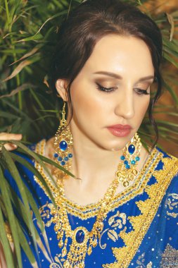 Hint kadın kostümü. Mavi Hint elbisesi giymiş genç güzel bir kadın çok renkli kahverengi arka planda, palmiye ağacıyla yakın çekim yapıyor..