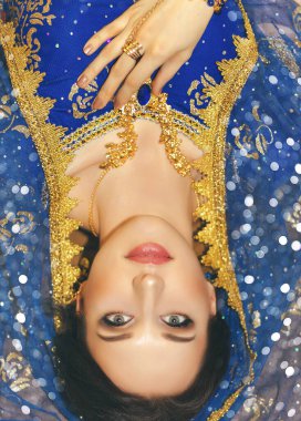 Hint kadın kostümü. Mavi Hint elbisesi giymiş genç güzel bir kadın çok renkli kahverengi arka planda yakın çekim yapıyor..