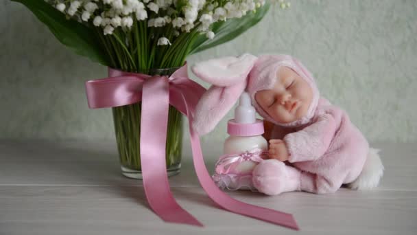 Oyuncak Bebek süt ile çiçek yakınındaki bir masaya oturur. Bebek duş için. Tematik Doğum günü dekorasyonu için — Stok video