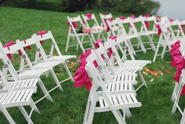 Krzesła ślubne z wstążkami stanąć w parku na trawie w ogrodzie — Zdjęcie stockowe