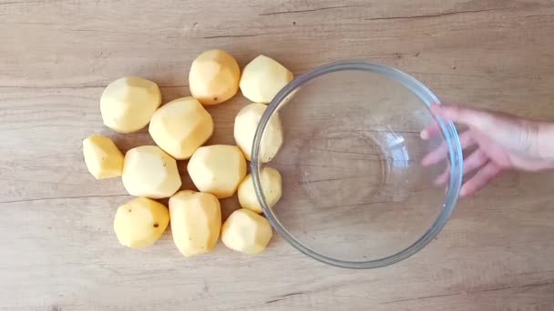 Handen zetten schone geschilde aardappelen in een glazen kom op een tabel, een recept (bovenaanzicht) — Stockvideo