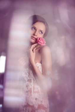 Moda gelin. Genç güzel kız mükemmel cilt ile model ve makyaj, gelinlik rhinestones ve dantel, saçları çiçekler. cam lamba parlama. Yumuşak odak, tonlama